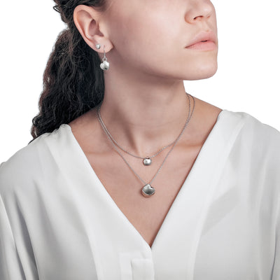 Person in white top wearing two Lumoava Hug necklaces