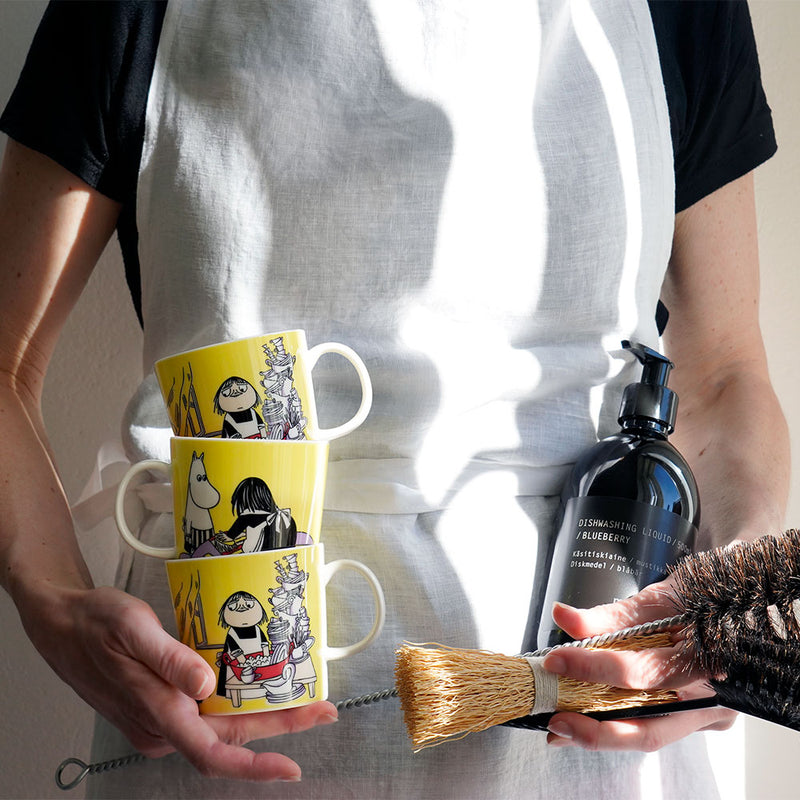 woman holding misabel mugs in right hand and cleaning supplies in left
