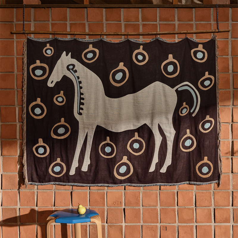 Marimekko Musta Tamma Blanket hanging in front of brick wall