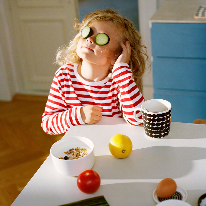 Child acting silly at dinner table next to Rasymatto mug