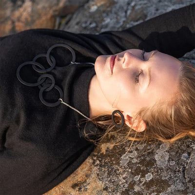 Woman laying on rocky surface wearing Valona Korona Birch Stud Earrings, Black