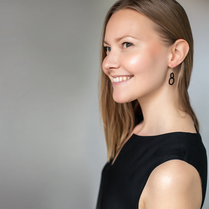Smiling woman in black top wearing Valona Mini Halo Birch Earrings, Black